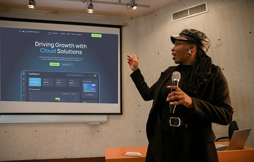 A person holding a microphone is giving a presentation next to a large screen displaying a slide about cloud solutions from a company named Cloudsprout.