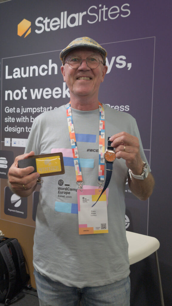 A person wearing glasses and a flat cap smiling at a tech conference, holding a trophy card and a watch, standing in front of a 'Stellar Sites' backdrop.