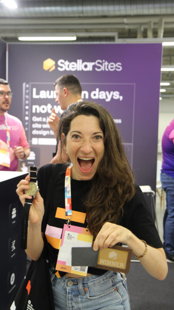 A woman smiling and holding a watch and a 'Winner' card at a tech event, standing in front of a Stellar Sites banner.